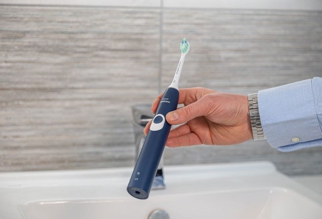 Hand holding an electric toothbrush over a sink