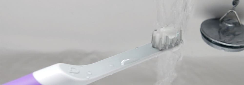 Brush under running tap with toothpaste on head