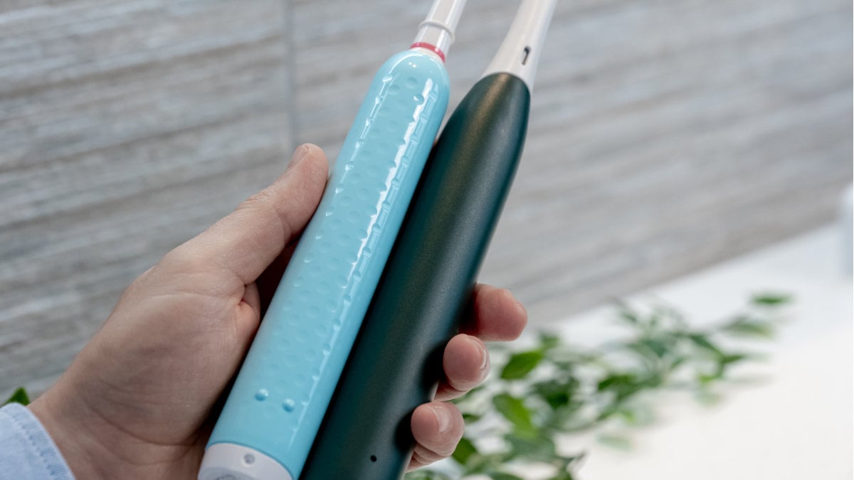 Oral-B iO2 and Oral-B Pro 1 Series being held next to each other in a single hand to compare the texture on their reverse