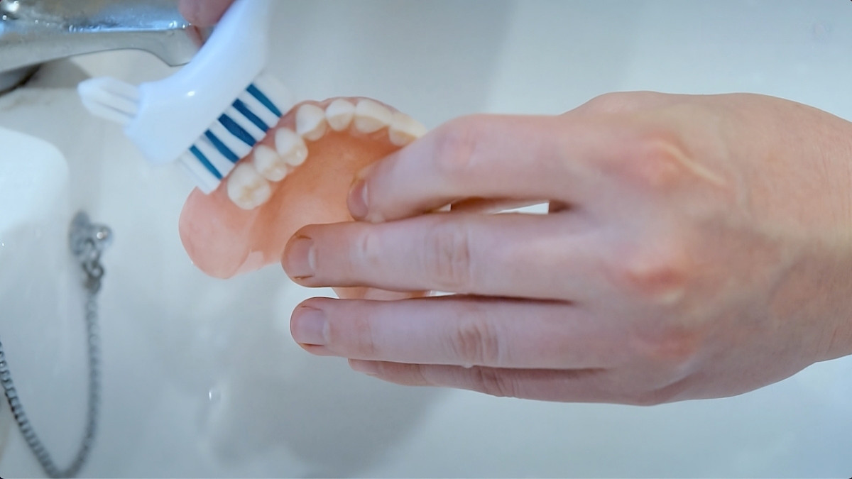 Dentures being cleaned with denture brush