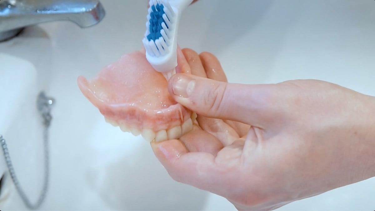 Denture brush being used to clean denture